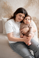 baby and mother, mom hugging baby at home, maternal love and care, mom with a small child, brown or beige background