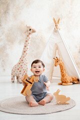 a smiling baby plays in a children's room with soft toys and a teepee, and a cute baby in a gray cotton bodysuit plays with a wooden car on the floor