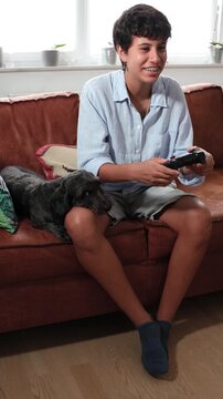 Teenager girl playing a video game on the console while sitting on the sofa with a pet dog