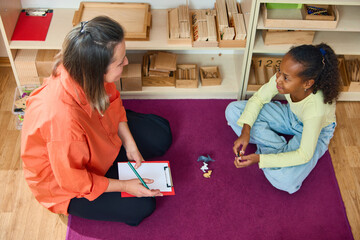 Psychologist and girl sitting on floor during therapy session. Concept of child psychology,...