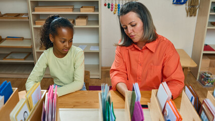 Teacher supporting girl during classroom activity with learning materials. Concept of education,...