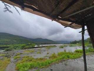 Obraz premium Scenic View of River, Green Hills, and Cloudy Mountains from a Hut