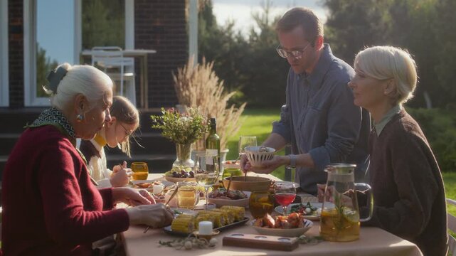 Caring middle-aged Caucasian man serving appetizer to senior woman at family dinner on lovely fall weekend, spending time together outdoors in cozy cottage backyard