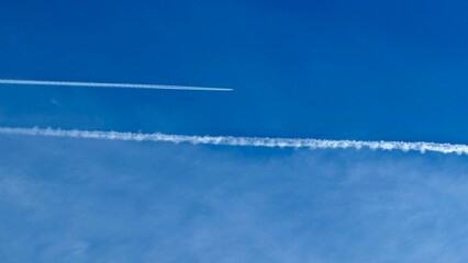 clear blue sky with two white contrails left by airplanes. These contrails are formed when hot, moist exhaust from jet engines mixes with cold, dry air at high altitudes, causing water vapor to conden
