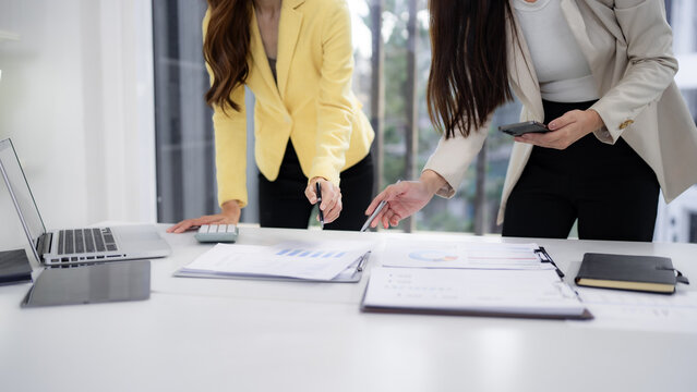 Adult Asian businesswomen collaborate data analysis strategic plan review financial reports discuss market trends modern office workspace - Powered by Adobe