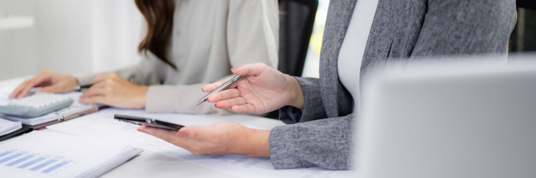 Professional adult Asian businesswomen collaborate discussing financial reports analyzing market strategy in a modern office setting - Powered by Adobe
