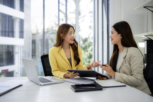 Asian businesswomen adult professionals discuss business strategy collaborate on project exchange ideas share insights achieve success modern bright office workspace