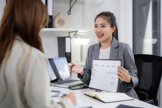 Asian business women professionals discuss financial reports analyze data collaborate in modern office setting for effective teamwork