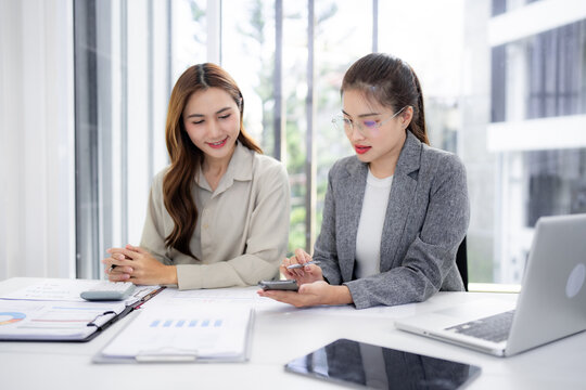 Adult Asian businesswomen professionals discuss analyze strategy collaborate share ideas using smartphone laptop office corporate workspace financial report planning