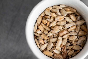 Close-up of shelled sunflower seeds in a white bowl on dark background. Healthy snack, natural texture, suitable for nutrition, food, and lifestyle themes.