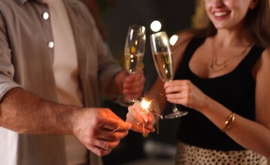Friends celebrating New Year with sparklers and wine glasses indoors, closeup