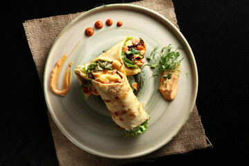 Overhead shot of two gourmet vegan wraps or burritos with microgreens and colorful filling, elegantly plated with sauce swirls and drops. Healthy and plant-based meal.