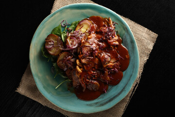 Vegan delight. Overhead shot of a rich, savory vegan mushroom stew or goulash with roasted potatoes and red onion, served on a stunning turquoise plate and burlap.