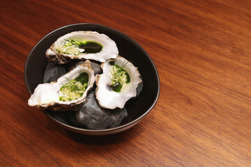 Three fresh oysters on the half shell, garnished with dill and green oil, artfully presented on...