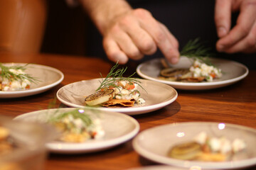 A chef's hand garnish a row of gourmet appetizers with fresh dill or herbs on elegant plates....
