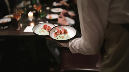 Waiter bringing out two bowls of a crudo dish on one hand during busy seafood night at the restaurant.