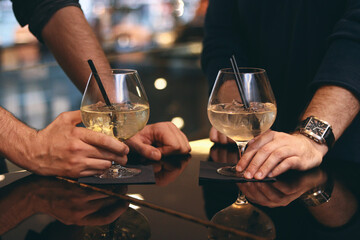 wo people toasting with white wine spritzers or cocktails in elegant balloon glasses at a dark,...