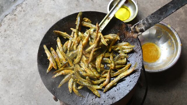Small Snakehead or Channa orientalis Fish being fried in a pan. Fish are typically marinated with spices like turmeric, salt, and chili powder before being deep fried until they are crispy and golden.