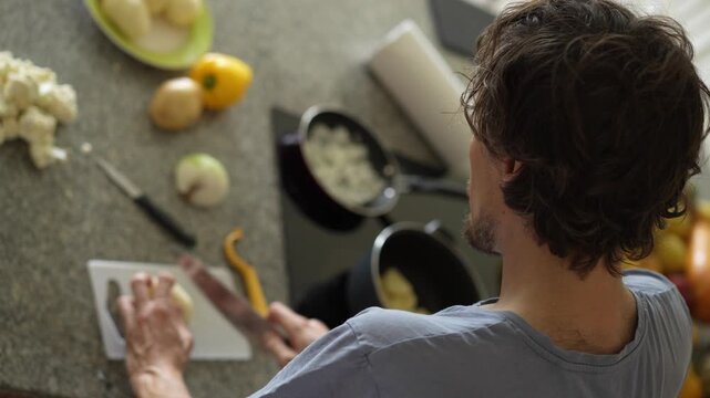 A young man is cooking food in the kitchen, focusing on preparing a delicious homemade meal. A relatable and warm moment of homemaking, creativity, and culinary enjoyment in a cozy setting.