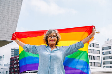 Senior woman proudly showing rainbow pride flag in city
