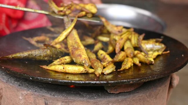 Small Snakehead or Channa orientalis Fish being fried in a pan. Fish are typically marinated with spices like turmeric, salt, and chili powder before being deep fried until they are crispy and golden.