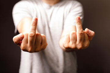 Close-up of a person's hands making the middle finger gesture, a symbol of defiance, rudeness, or...