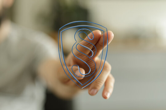 Digital concept of legal protection. A hand interacts with a virtual shield displaying a paragraph symbol, representing law, justice, and regula
