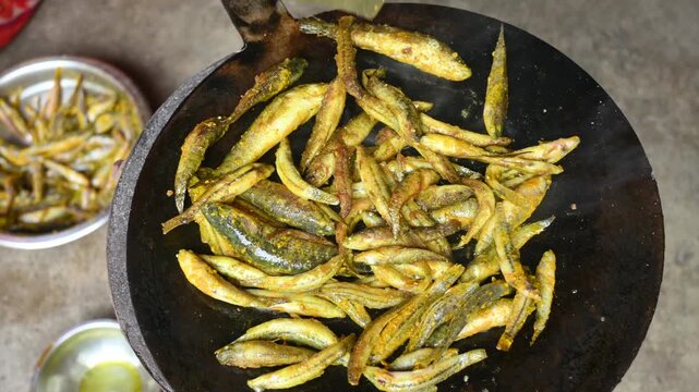 Small Snakehead or Channa orientalis Fish being fried in a pan. Fish are typically marinated with spices like turmeric, salt, and chili powder before being deep fried until they are crispy and golden.
