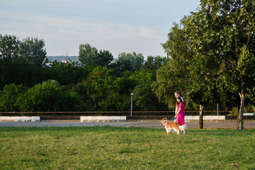 Fototapeta premium Couple enjoying a summer walk with their dog in the park, surrounded by green trees and nature. Side view portrait of happy young family