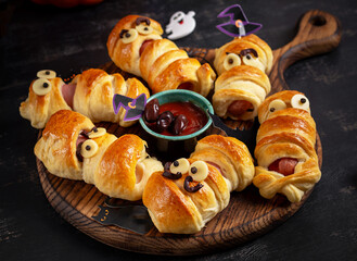 Halloween food. Scary sausage mummies in dough with funny eyes on dark background.