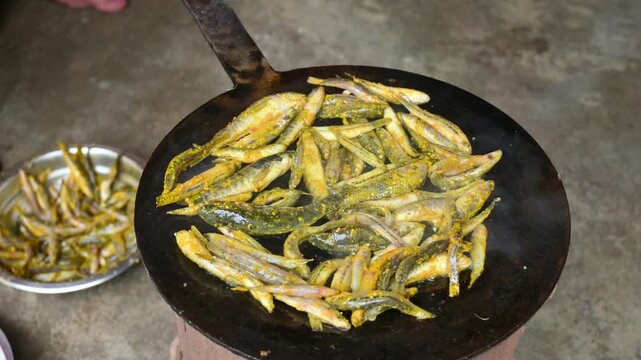 Small Snakehead or Channa orientalis Fish being fried in a pan. Fish are typically marinated with spices like turmeric, salt, and chili powder before being deep fried until they are crispy and golden.