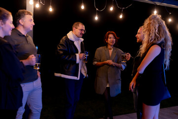 Group of friends socializing outdoors under string lights at nighttime