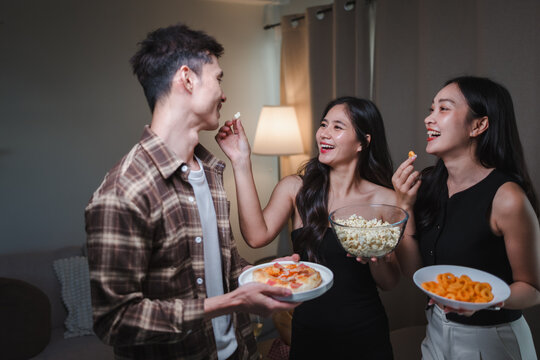 Young Asian friends having fun sharing snacks at home party - Powered by Adobe