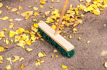 Pile of Golden Autumn Leaves on a Pavement with a Broom and Garbage Bag