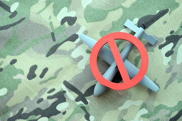 Unnamed grey toy drone model and red prohibition sign on camouflage fabric. Anti-aircraft warfare