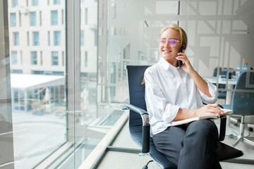Smiling woman talking on the phone while sitting in a modern office