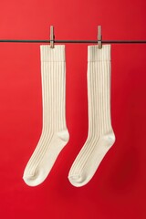 Cream-colored ribbed socks hanging on clips against bright red background, ideal for fashion, retail, minimalist styling, and product display themes