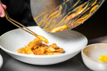 Chef plating hot gnocchi pasta with creamy tomato sauce and mushrooms into a white bowl using tongs. Steam rises from the pan, highlighting freshness and texture.
