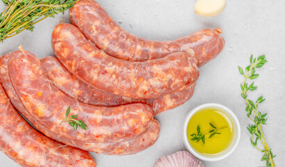 Raw pork sausages with spices, garlic, thyme, and olive oil on light background. Fresh homemade sausage, uncooked meat, organic food ingredient for barbecue and grill