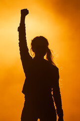 Strong woman raises her hand in triumph, silhouetted against twilight glow, women’s rights, women’s day, international women’s day, women empowerment, equality, female empowerment