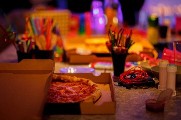 Open pizza box on a table at a creative party with colorful art supplies and vibrant lights
