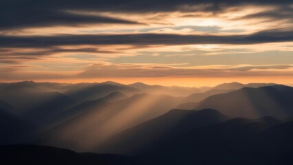 Fototapeta premium A mountain range is bathed in sunlight filtering through clouds at sunset