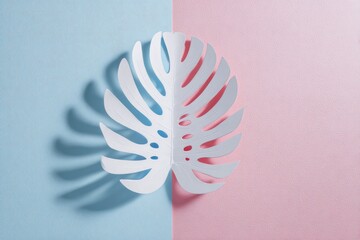 A paper monstera leaf casting a shadow against a two-tone pastel blue and pink backdrop