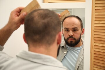 Fototapeta premium Baldness problem. Man brushing his hair with comb near mirror at home