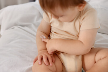 Cute baby with cream on his arm at home, closeup