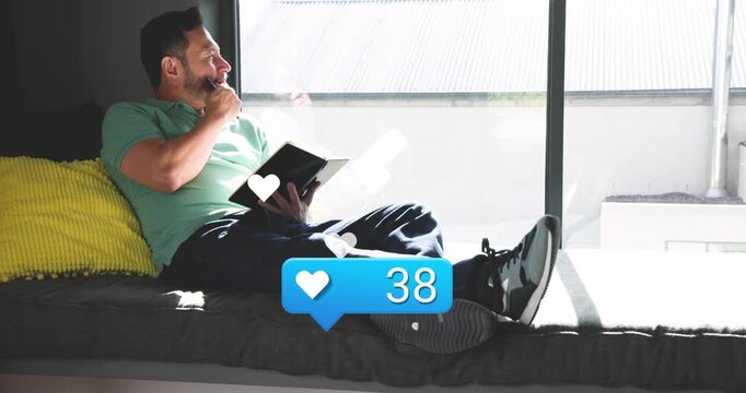 Mature man reading book on window bench initiating social media heart counter rising to ninety-five