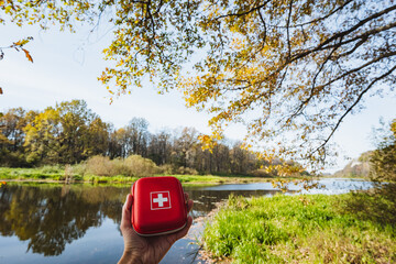 A hiker stands by a riverbank with a first aid kit, surrounded by colorful autumn leaves, highlighting adventure, care, and the importance of preparedness in exploring natures beauty