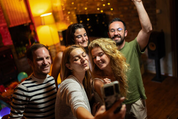 Group of friends capturing a cheerful selfie at a lively indoor social gathering