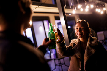 Friends toasting with drinks at a nighttime outdoor gathering with festive lighting