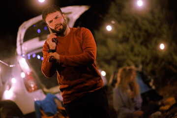 Friend talks on phone at night camp setting with warm lights and relaxed atmosphere